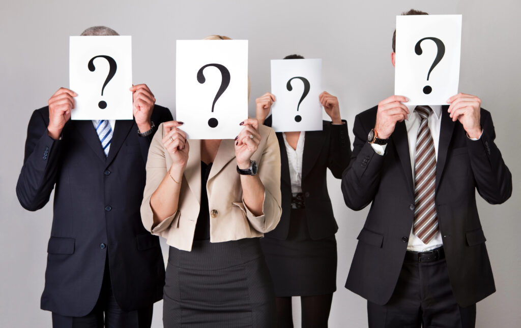 Group of 4 unidentified business people holding a white sheet of paper with a question mark covering their faces to denote the impact of meritocracy.