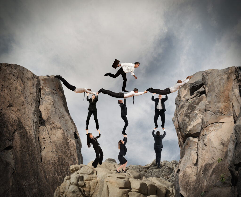 six individuals hold up three individuals hanging onto two ends of a mountain while one man walks on their backs.